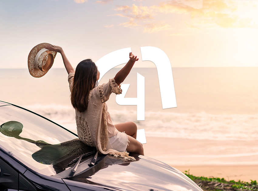 Woman sitting on car holding her hands in the sky and looking at the sunset on a beach.